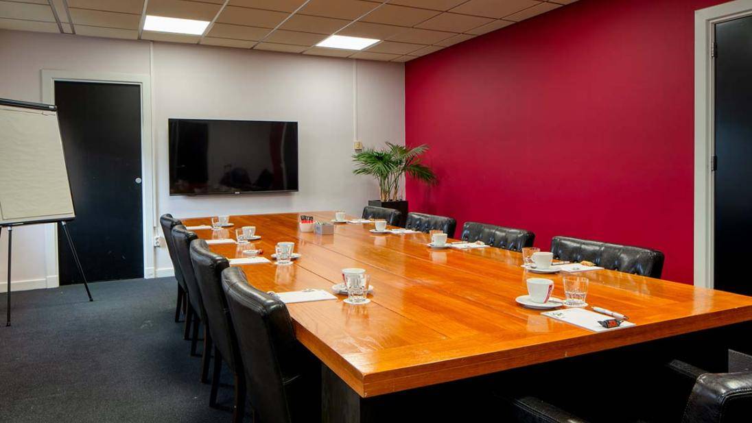 Grote vergaderruimte met rode muur tafel en stoelen schuin van voren